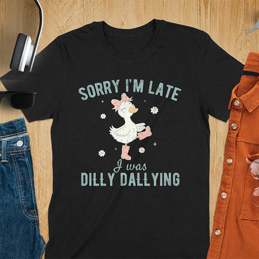 A t-shirt with a white goose wearing pink boots and a pink bow, surrounded by small flowers. Text: SORRY I'M LATE above and I was DILLY DALLYING below. This cute geese t shirt features goose cuteness and kawaiiness cuteness. A snarky humorous and sarcastic meme shirt about dilly dallying. A funny genz meme with funny animals and spring flowers. This silly funny goose design has vintage aesthetics and is an animal person gift or mom gift.
