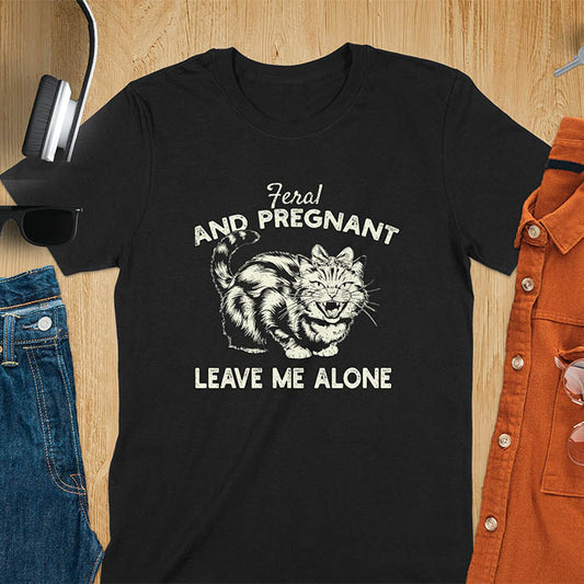 A t-shirt with a tabby cat with a grumpy expression and a pink bow. Text: Feral AND PREGNANT above and LEAVE ME ALONE below. This funny maternity tee is a feral cats shirt for a mom to be shirt. A pregnancy humor design for a pregnancy announce or sibling pregnancy. An expecting mom gift or mommy to be gift, a maternity apparel and pregnancy keepsake for an expecting baby during a feral pregnancy.