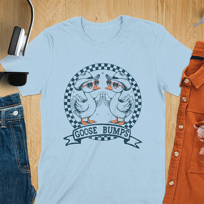 A t-shirt with two geese in cowboy hats and heart sunglasses, within a checkered circle, touching wings. Banner reads "GOOSE BUMPS". This Retro Goose Bump Shirt is a sarcastic goose, silly goose crewneck, Funny Sarcastic Silly Meme Tee. An unhinged tee, weirdcore meme, Snarky Sassy Saying Tee-shirt. A Hilarious Tshirt Gift, gift for goose lover, cowboy cowgirl gift, animal person, gift mom hers, cute animal clothe. Features kawaiiness cuteness.