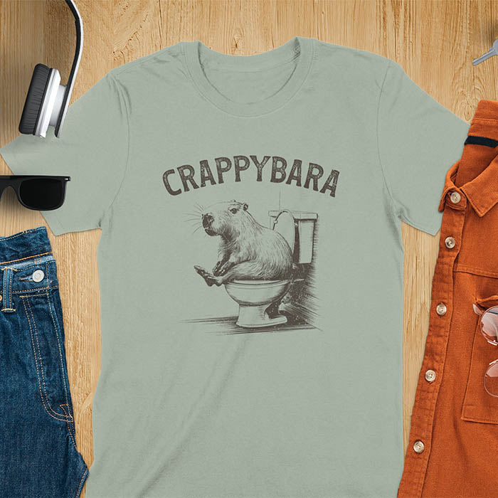 A t-shirt with a capybara on a toilet. Text: "CRAPPYBARA". This Crappybara Tshirt is an inappropriate shirt, offensive shirt & Toilet Humor Gag Gift. A Funny Meme Tee-shirt, Trending meme shirt, genz gen z weirdcore t-shirt. Features Kawaiiness Kawaiiful, Capybara cuteness, Weird capybara gift, Funny Vintage Capybara Shirt. For animal person gift, pet lovers tee, Animal Lover T-shirt, gift mom hers. A Y2K tee-shirt, Vintage Silly Party Tees, shirts that go hard.