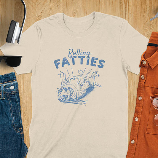 A t-shirt with a basset hound dog on its back getting a belly rub. Text: "Rolling FATTIES". This Rolling Fatties Dog Shirt is a Basset Hound Owner T-shirt, basset hound tee. A Funny Graphic Tee for Dog cuteness gift, Doggy doggie gift, Kawaii Cute Fat Puppy. Perfect gift for dog lover, Dog dad shirt, Dog mama shirt, Dog owner tshirt, pet vintage shirt, Pet lover apparel, Animal Lover Gift, Dog person clothe, Gift mom hers. An Unhinged Tee-shirt, Retro dog shirt, Vintage dog tee.