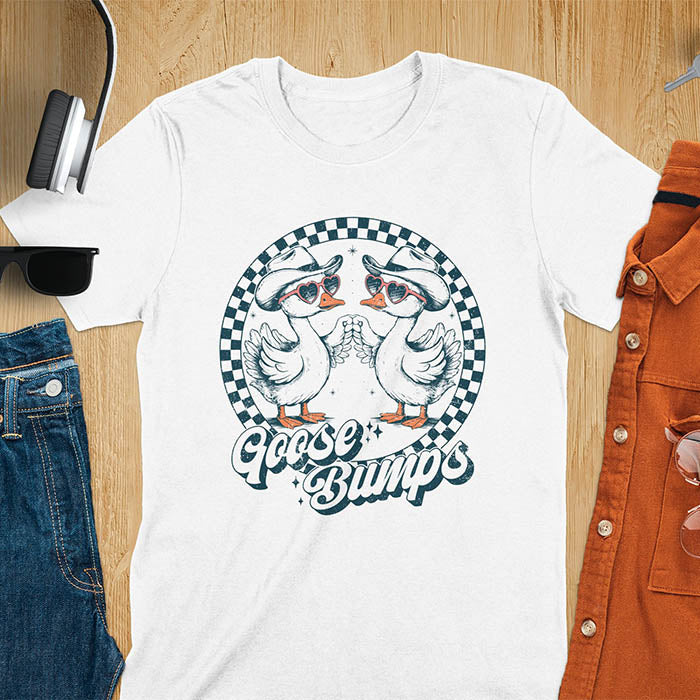A t-shirt with two geese in cowboy hats and heart sunglasses touching hands, inside a checkered circle. Text "Goose Bumps" is below them on a curved banner. A silly goose crewneck, sarcastic, Funny Sarcastic Meme Tee-shirt, Retro Western Goose Shirt, Snarky Sassy Saying Tshirt, unhinged tee-shirt, weirdcore meme. Ideal gift for goose lover, cowboy cowgirl gift, animal person, gift mom hers. Features kawaiiness cuteness, cute animal clothe, Vintage Silly Humorous Tee Gift.