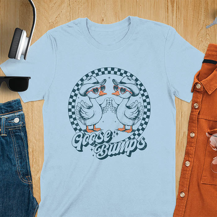 A t-shirt with two geese in cowboy hats and heart sunglasses touching hands, inside a checkered circle. Text "Goose Bumps" is below them on a curved banner. A silly goose crewneck, sarcastic, Funny Sarcastic Meme Tee-shirt, Retro Western Goose Shirt, Snarky Sassy Saying Tshirt, unhinged tee-shirt, weirdcore meme. Ideal gift for goose lover, cowboy cowgirl gift, animal person, gift mom hers. Features kawaiiness cuteness, cute animal clothe, Vintage Silly Humorous Tee Gift.
