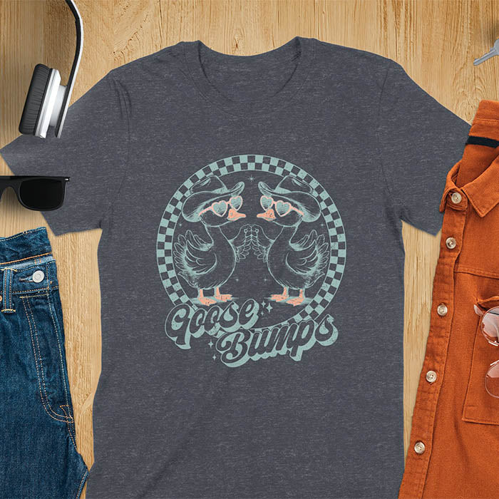 A t-shirt with two geese in cowboy hats and heart sunglasses touching hands, inside a checkered circle. Text "Goose Bumps" is below them on a curved banner. A silly goose crewneck, sarcastic, Funny Sarcastic Meme Tee-shirt, Retro Western Goose Shirt, Snarky Sassy Saying Tshirt, unhinged tee-shirt, weirdcore meme. Ideal gift for goose lover, cowboy cowgirl gift, animal person, gift mom hers. Features kawaiiness cuteness, cute animal clothe, Vintage Silly Humorous Tee Gift.
