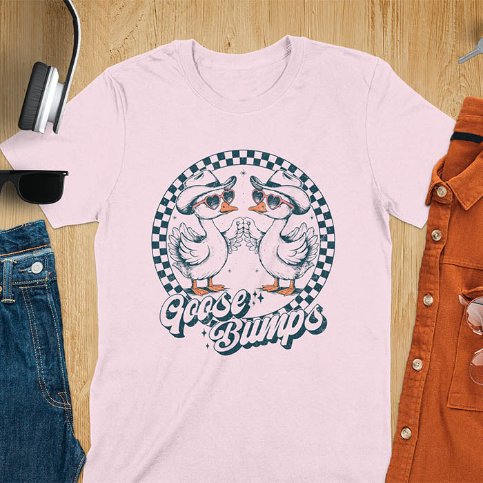 A t-shirt with two geese in cowboy hats and heart sunglasses touching hands, inside a checkered circle. Text "Goose Bumps" is below them on a curved banner. A silly goose crewneck, sarcastic, Funny Sarcastic Meme Tee-shirt, Retro Western Goose Shirt, Snarky Sassy Saying Tshirt, unhinged tee-shirt, weirdcore meme. Ideal gift for goose lover, cowboy cowgirl gift, animal person, gift mom hers. Features kawaiiness cuteness, cute animal clothe, Vintage Silly Humorous Tee Gift.