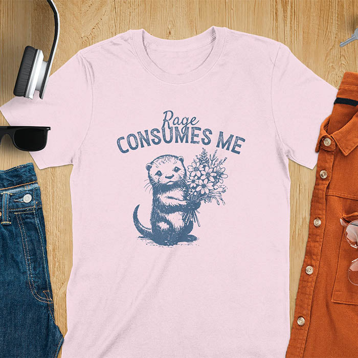 A t-shirt with an otter holding flowers. Text: "Rage CONSUMES ME" above. This dark humor tee features otter cuteness and cuteness kawaii, a mental health meme. A genz meme gift and weird funny t shirt, a funny gag gift or animal lover gag. One of those shirts that go hard, an unhinged tshirt. A mom gift hers or animal person gift with a retro graphic tee style.