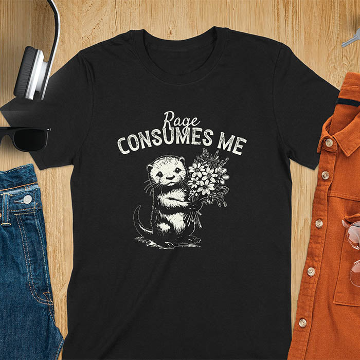 A t-shirt with an otter holding flowers. Text: "Rage CONSUMES ME" above. This dark humor tee features otter cuteness and cuteness kawaii, a mental health meme. A genz meme gift and weird funny t shirt, a funny gag gift or animal lover gag. One of those shirts that go hard, an unhinged tshirt. A mom gift hers or animal person gift with a retro graphic tee style.