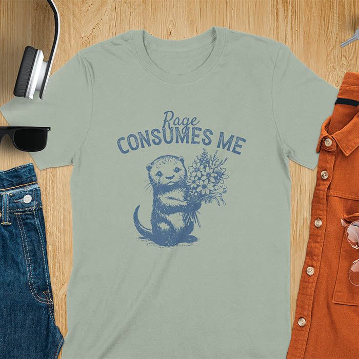 A t-shirt with an otter holding flowers. Text: "Rage CONSUMES ME" above. This dark humor tee features otter cuteness and cuteness kawaii, a mental health meme. A genz meme gift and weird funny t shirt, a funny gag gift or animal lover gag. One of those shirts that go hard, an unhinged tshirt. A mom gift hers or animal person gift with a retro graphic tee style.