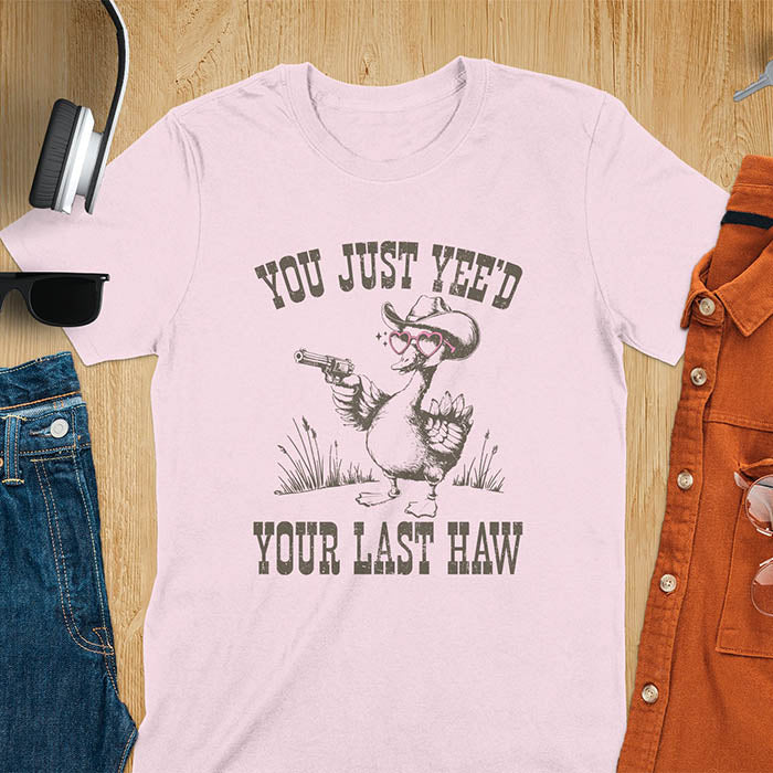 A t-shirt with a goose wearing a cowboy hat and sunglasses, holding a pistol. Text: "YOU JUST YEE'D" above and "YOUR LAST HAW" below. This funny western shirt features a silly goose shirt or goose lovers gift. A cowboy tshirt or cowgirl shirt, a western style tee and western shirt. A retro graphic tee and weirdcore tshirt, an animal person gift or animal lover gag. A mom gift alternative.