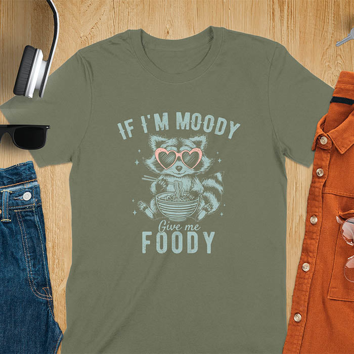 A t-shirt: raccoon in heart sunglasses with noodles. Text: "IF I'M MOODY Give me FOODY". A Funny Raccoon T-shirt, funny trash panda, Vintage Trash Panda Tee. Sarcastic Saying Tee-shirt, snarky humorous, trending funny shirt, meme t shirt, Gag Gift. Features kawaiiness cuteness. Great gift for animal person, Animal Lover Tshirt, mom. Retro aesthetic tee.