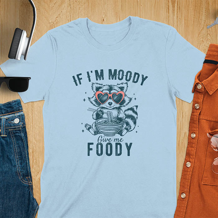 A t-shirt: raccoon in heart sunglasses with noodles. Text: "IF I'M MOODY Give me FOODY". A Funny Raccoon T-shirt, funny trash panda, Vintage Trash Panda Tee. Sarcastic Saying Tee-shirt, snarky humorous, trending funny shirt, meme t shirt, Gag Gift. Features kawaiiness cuteness. Great gift for animal person, Animal Lover Tshirt, mom. Retro aesthetic tee.