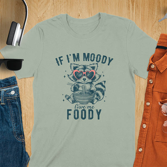 A t-shirt: raccoon in heart sunglasses with noodles. Text: "IF I'M MOODY Give me FOODY". A Funny Raccoon T-shirt, funny trash panda, Vintage Trash Panda Tee. Sarcastic Saying Tee-shirt, snarky humorous, trending funny shirt, meme t shirt, Gag Gift. Features kawaiiness cuteness. Great gift for animal person, Animal Lover Tshirt, mom. Retro aesthetic tee.