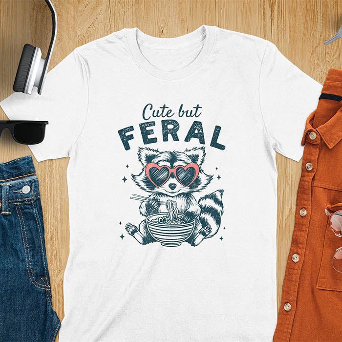A t-shirt with a raccoon in heart sunglasses eating ramen. Text: "Cute but FERAL". A Funny Cute But Feral Raccoon Shirt, Vintage Retro Graphic Ramen Tee, Silly Sarcastic Tshirt, Hilarious Gag Gift. Unhinged, trash panda, trendy design. Features kawaiiness cuteness. Great gift for animal person, raccoon lover, mom, feral mom. Vintage inspired Animal Lover T-shirt, almost feral shirt.