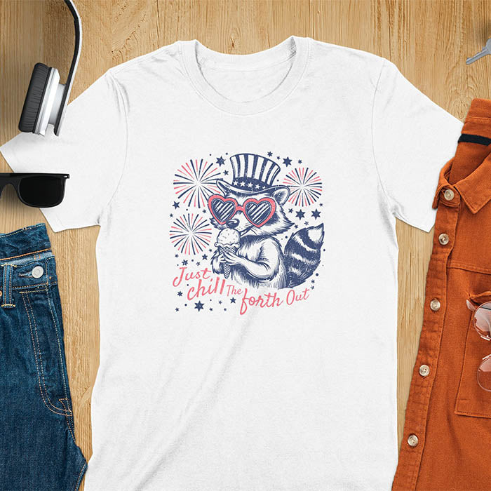 A t-shirt with a raccoon in a patriotic top hat & heart sunglasses, holding an ice cream cone. Fireworks burst around it. Text: "JUST CHILL THE FOURTH OUT". This raccoon cuteness tee is a funny 4th of July fourth of july shirt for chill the 4th out. A fireworks shirt, patriotic merica tee & freedom t shirt for independence day. Has vintage aesthetics, a funny patriot animal person gift or mom gift among 4th of july shirts.