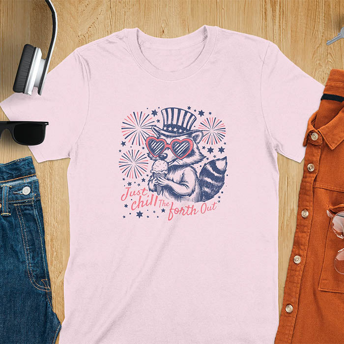 A t-shirt with a raccoon in a patriotic top hat & heart sunglasses, holding an ice cream cone. Fireworks burst around it. Text: "JUST CHILL THE FOURTH OUT". This raccoon cuteness tee is a funny 4th of July fourth of july shirt for chill the 4th out. A fireworks shirt, patriotic merica tee & freedom t shirt for independence day. Has vintage aesthetics, a funny patriot animal person gift or mom gift among 4th of july shirts.