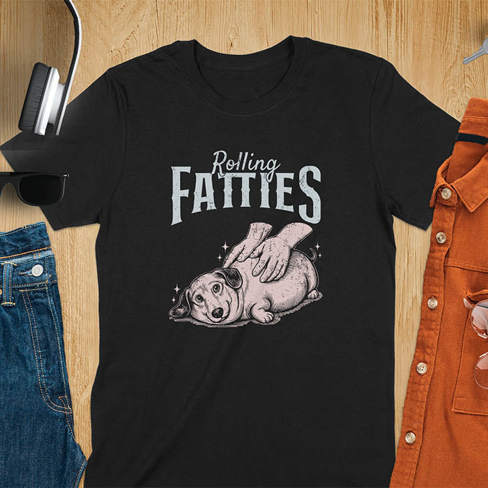 A t-shirt with a retro dog graphic of a dachshund (a doxie or sausage dog pet) lying on its side, happily getting its body rubbed by a pair of human hands. Above the dog, the text reads "Rolling FATTIES". This dog cuteness gift has a vintage aesthetic, perfect for a dog person clothe, dog dad shirt, dachshund mom, or animal person gift. A silly funny shirt for dog pet lovers looking for an animal gag gift or funny memes shirts.