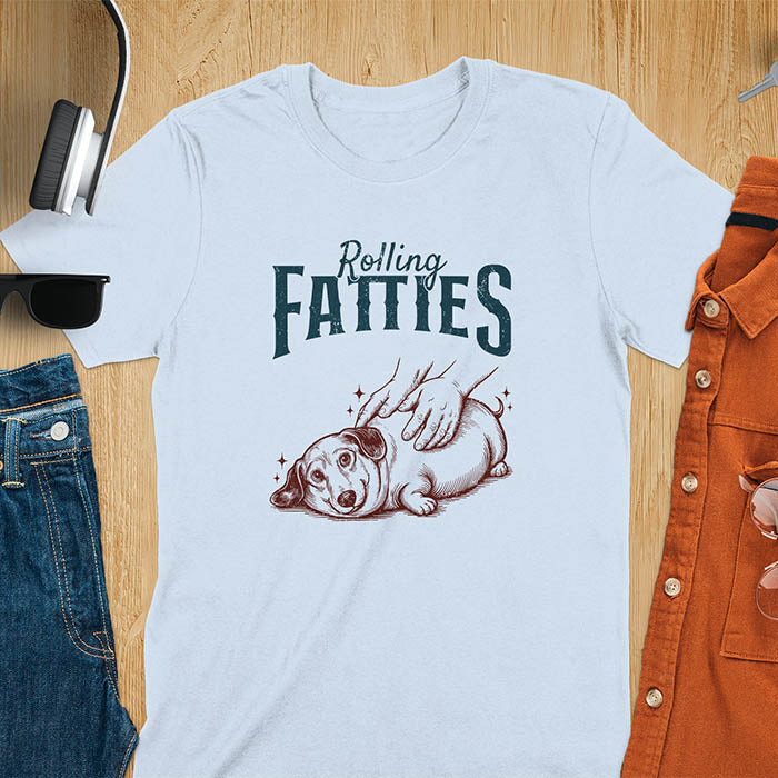 A t-shirt with a retro dog graphic of a dachshund (a doxie or sausage dog pet) lying on its side, happily getting its body rubbed by a pair of human hands. Above the dog, the text reads "Rolling FATTIES". This dog cuteness gift has a vintage aesthetic, perfect for a dog person clothe, dog dad shirt, dachshund mom, or animal person gift. A silly funny shirt for dog pet lovers looking for an animal gag gift or funny memes shirts.