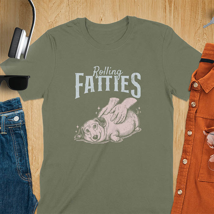 A t-shirt with a retro dog graphic of a dachshund (a doxie or sausage dog pet) lying on its side, happily getting its body rubbed by a pair of human hands. Above the dog, the text reads "Rolling FATTIES". This dog cuteness gift has a vintage aesthetic, perfect for a dog person clothe, dog dad shirt, dachshund mom, or animal person gift. A silly funny shirt for dog pet lovers looking for an animal gag gift or funny memes shirts.