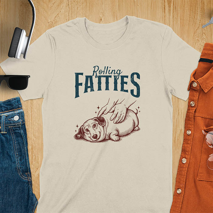 A t-shirt with a retro dog graphic of a dachshund (a doxie or sausage dog pet) lying on its side, happily getting its body rubbed by a pair of human hands. Above the dog, the text reads "Rolling FATTIES". This dog cuteness gift has a vintage aesthetic, perfect for a dog person clothe, dog dad shirt, dachshund mom, or animal person gift. A silly funny shirt for dog pet lovers looking for an animal gag gift or funny memes shirts.
