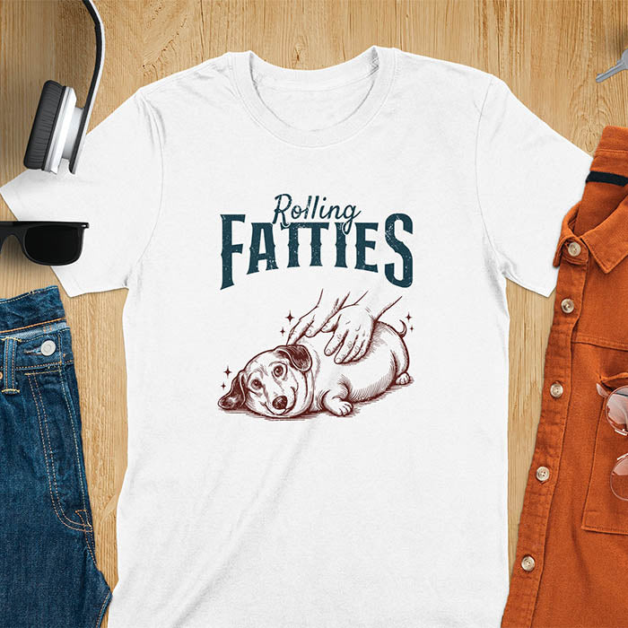 A t-shirt with a retro dog graphic of a dachshund (a doxie or sausage dog pet) lying on its side, happily getting its body rubbed by a pair of human hands. Above the dog, the text reads "Rolling FATTIES". This dog cuteness gift has a vintage aesthetic, perfect for a dog person clothe, dog dad shirt, dachshund mom, or animal person gift. A silly funny shirt for dog pet lovers looking for an animal gag gift or funny memes shirts.