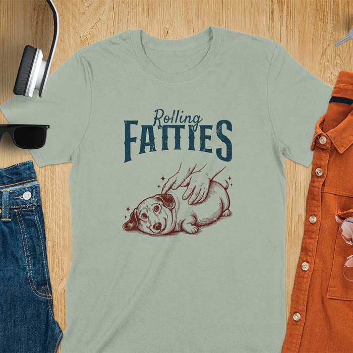 A t-shirt with a retro dog graphic of a dachshund (a doxie or sausage dog pet) lying on its side, happily getting its body rubbed by a pair of human hands. Above the dog, the text reads "Rolling FATTIES". This dog cuteness gift has a vintage aesthetic, perfect for a dog person clothe, dog dad shirt, dachshund mom, or animal person gift. A silly funny shirt for dog pet lovers looking for an animal gag gift or funny memes shirts.