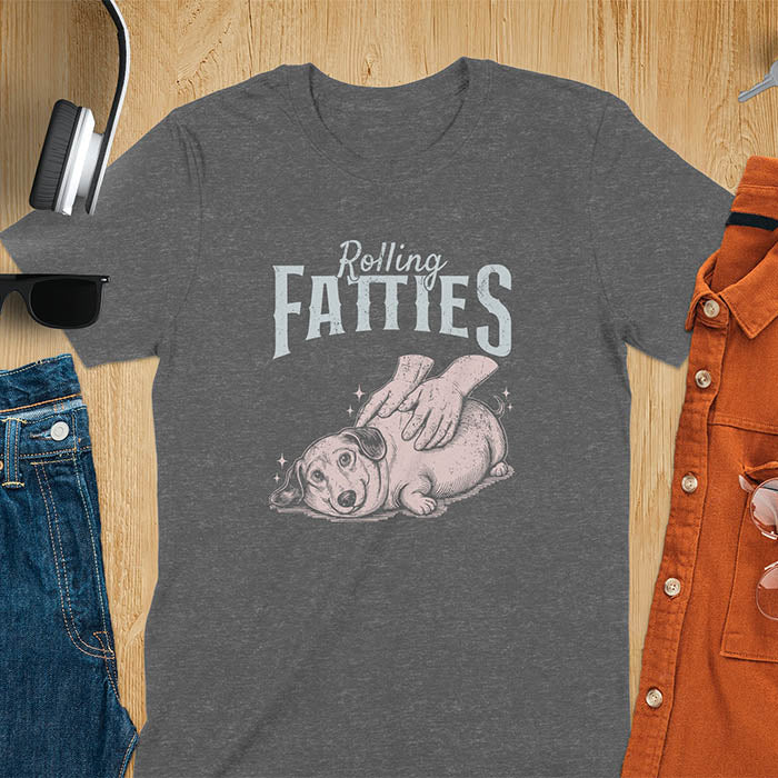 A t-shirt with a retro dog graphic of a dachshund (a doxie or sausage dog pet) lying on its side, happily getting its body rubbed by a pair of human hands. Above the dog, the text reads "Rolling FATTIES". This dog cuteness gift has a vintage aesthetic, perfect for a dog person clothe, dog dad shirt, dachshund mom, or animal person gift. A silly funny shirt for dog pet lovers looking for an animal gag gift or funny memes shirts.