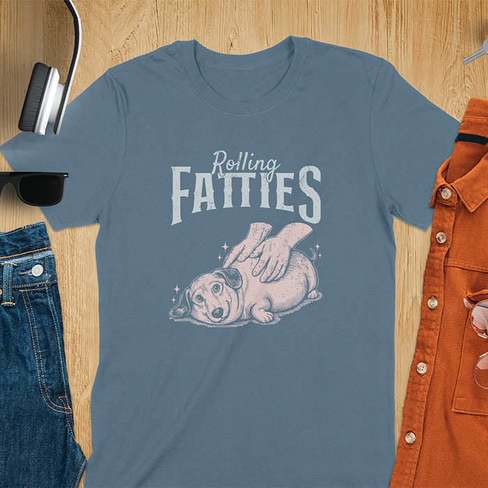 A t-shirt with a retro dog graphic of a dachshund (a doxie or sausage dog pet) lying on its side, happily getting its body rubbed by a pair of human hands. Above the dog, the text reads "Rolling FATTIES". This dog cuteness gift has a vintage aesthetic, perfect for a dog person clothe, dog dad shirt, dachshund mom, or animal person gift. A silly funny shirt for dog pet lovers looking for an animal gag gift or funny memes shirts.