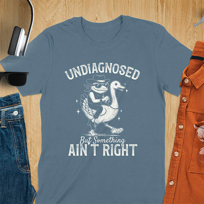Funny cowboy frog riding goose t-shirt in indigo blue featuring cartoon frog in cowboy hat and boots riding a goose with text 'UNDIAGNOSED - But Something AIN'T RIGHT