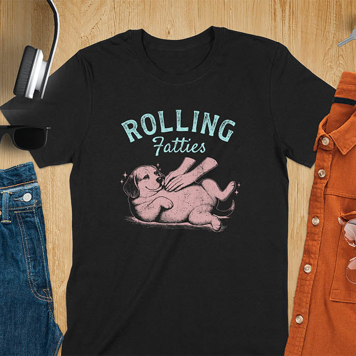 Black t-shirt featuring 'Rolling Fatties' text in teal lettering above a chubby beagle dog lying on its back in red/burgundy ink sketch style