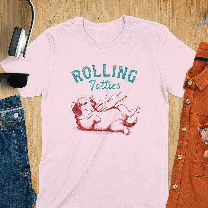 Light pink t-shirt featuring 'Rolling Fatties' text in teal lettering above a chubby beagle dog lying on its back in red/burgundy ink sketch style