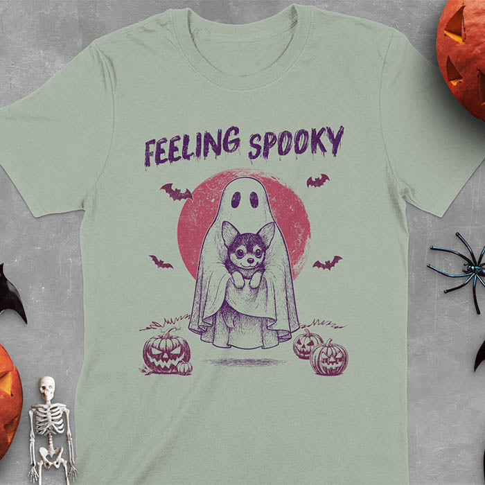 Sage green t-shirt featuring a ghost holding a corgi puppy with 'Feeling Spooky' text above, red moon background with bats and jack-o'-lanterns