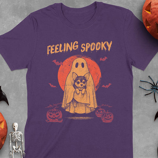Purple t-shirt featuring a ghost holding a corgi puppy with 'Feeling Spooky' text above, red moon background with bats and jack-o'-lanterns