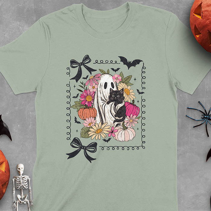 Sage green t-shirt featuring cute ghost holding black cat surrounded by pumpkins, bats, and floral elements in cottagecore coquette style