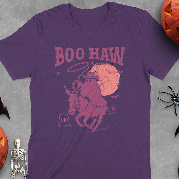 Purple t-shirt featuring cowboy ghost riding a donkey with lasso, 'BOO HAW' text above, red moon background with bats and RIP tombstone