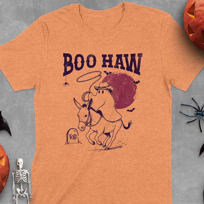 Heather Orange t-shirt featuring cowboy ghost riding a donkey with lasso, 'BOO HAW' text above, red moon background with bats and RIP tombstone