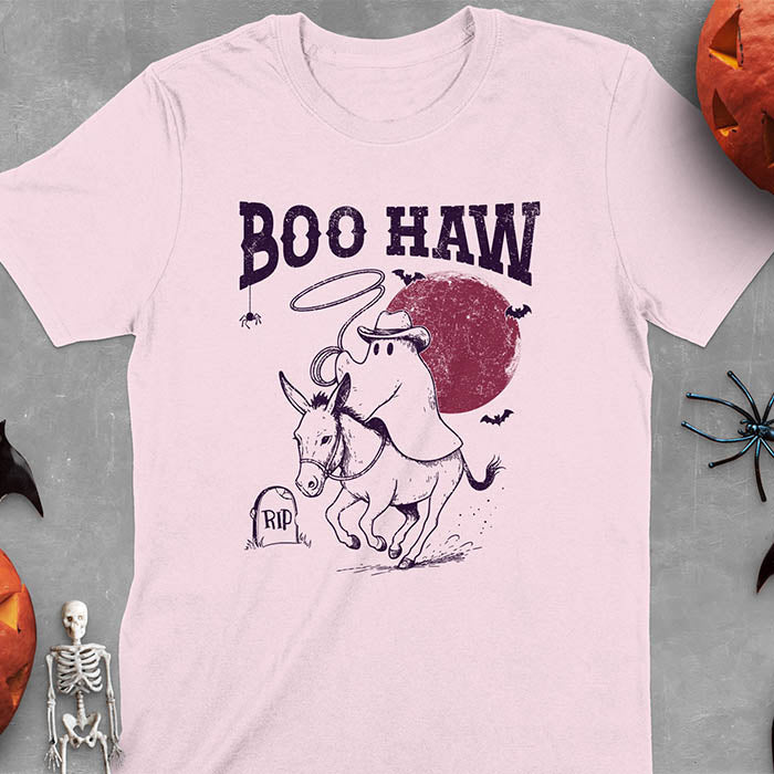 Light Pink t-shirt featuring cowboy ghost riding a donkey with lasso, 'BOO HAW' text above, red moon background with bats and RIP tombstone