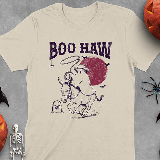 Sand color t-shirt featuring cowboy ghost riding a donkey with lasso, 'BOO HAW' text above, red moon background with bats and RIP tombstone