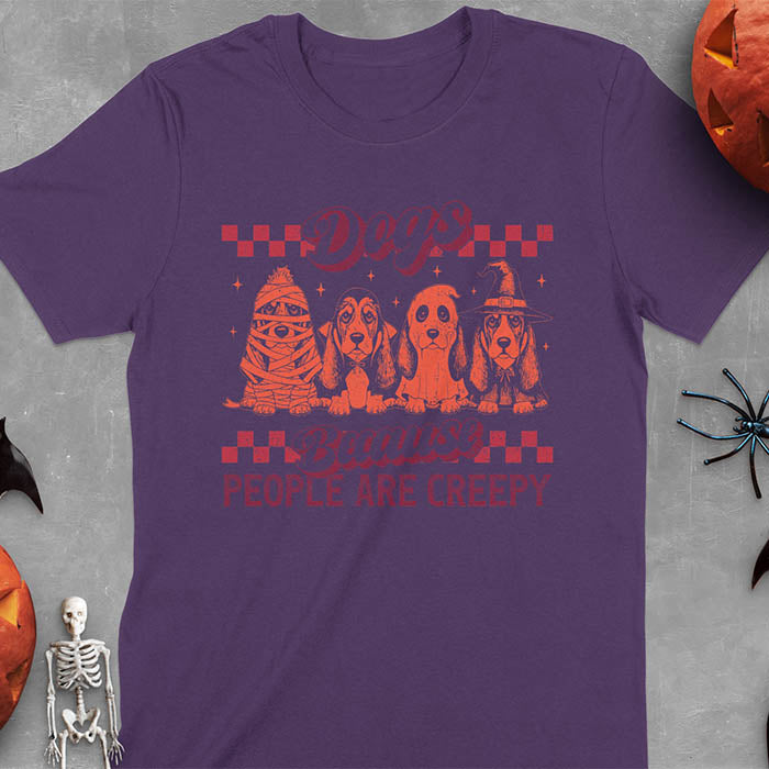 Purple t-shirt featuring four basset hounds in Halloween costumes - mummy, ghost, witch, and vampire - with 'Dogs Because People Are Creepy' text and checkered borders