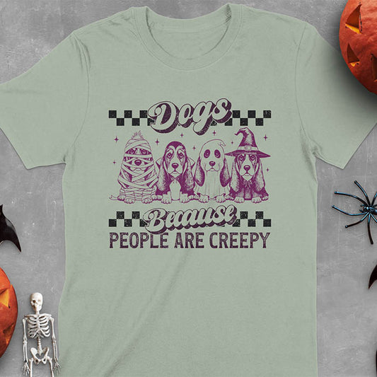 Sage green t-shirt featuring four basset hounds in Halloween costumes - mummy, ghost, witch, and vampire - with 'Dogs Because People Are Creepy' text and checkered borders