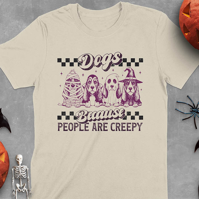 Sand color t-shirt featuring four basset hounds in Halloween costumes - mummy, ghost, witch, and vampire - with 'Dogs Because People Are Creepy' text and checkered borders