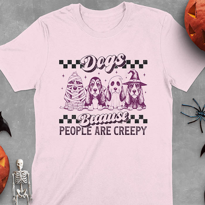 Light Pink t-shirt featuring four basset hounds in Halloween costumes - mummy, ghost, witch, and vampire - with 'Dogs Because People Are Creepy' text and checkered borders