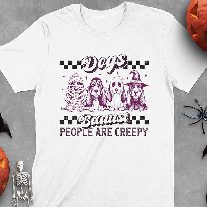 White t-shirt featuring four basset hounds in Halloween costumes - mummy, ghost, witch, and vampire - with 'Dogs Because People Are Creepy' text and checkered borders