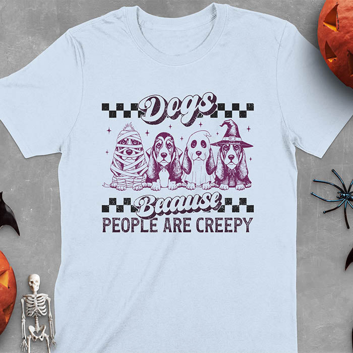 Light blue t-shirt featuring four basset hounds in Halloween costumes - mummy, ghost, witch, and vampire - with 'Dogs Because People Are Creepy' text and checkered borders