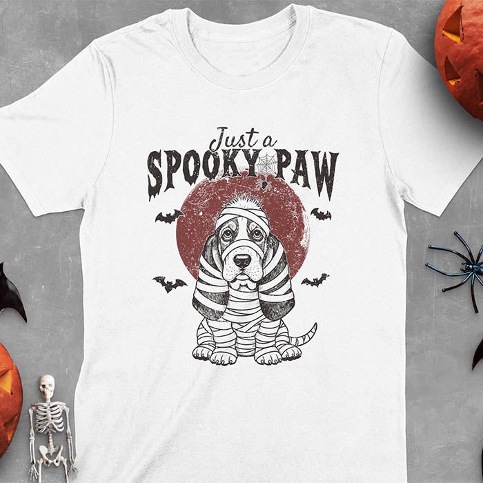 White t-shirt featuring cute a basset hound wrapped in white mummy bandages with 'Just a SPOOKY PAW' text above