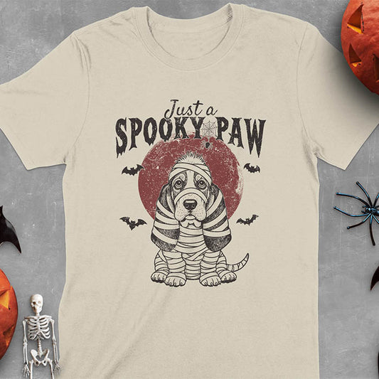 Sand color t-shirt featuring a cute basset hound wrapped in white mummy bandages with 'Just a SPOOKY PAW' text above
