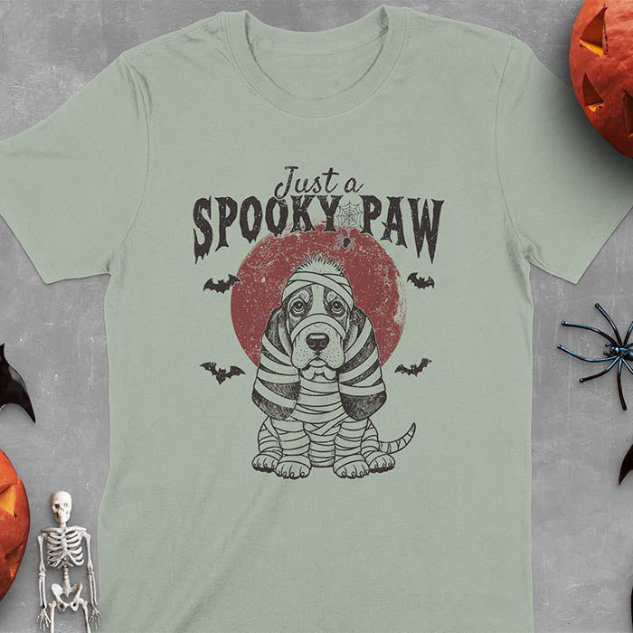 Sage green t-shirt featuring a cute basset hound wrapped in white mummy bandages with 'Just a SPOOKY PAW' text above