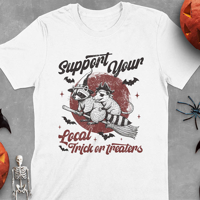 White t-shirt Halloween witch raccoon design featuring opossum pirate on broom with Support Your Local Trick or Treaters text
