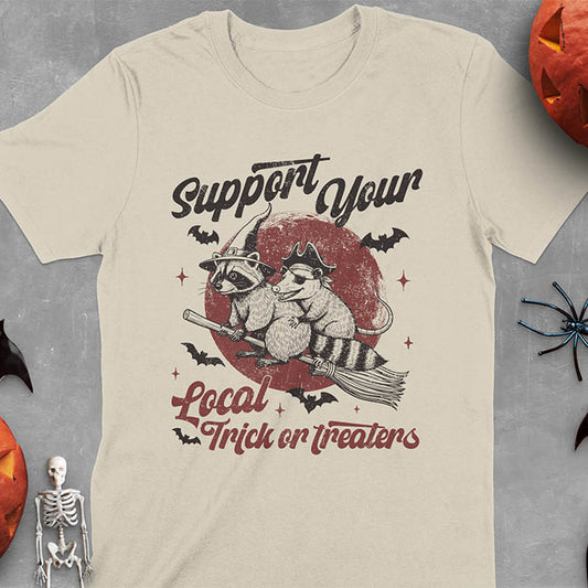 Sand colored t-shirt Halloween witch raccoon design featuring opossum pirate on broom with Support Your Local Trick or Treaters text