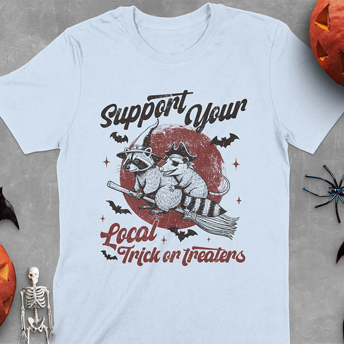 Light blue t-shirt Halloween witch raccoon design featuring opossum pirate on broom with Support Your Local Trick or Treaters text