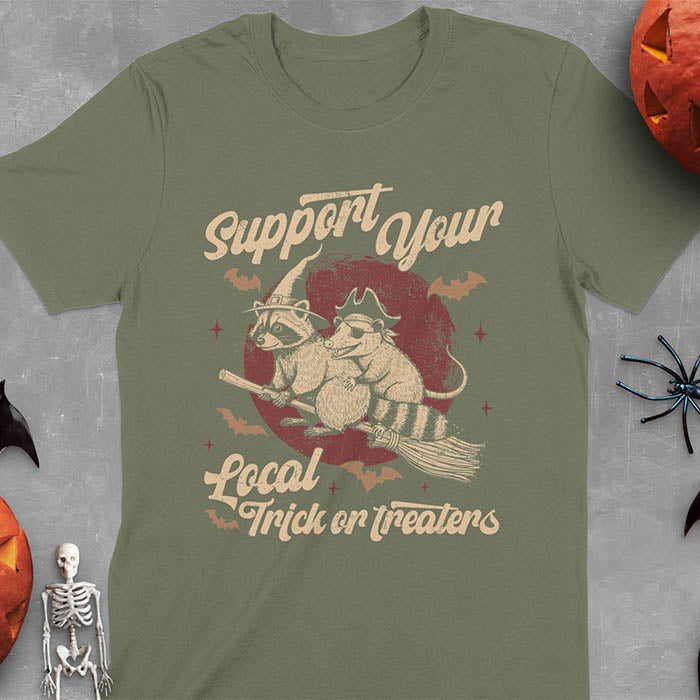 Military Green t-shirt Halloween witch raccoon design featuring opossum pirate on broom with Support Your Local Trick or Treaters text